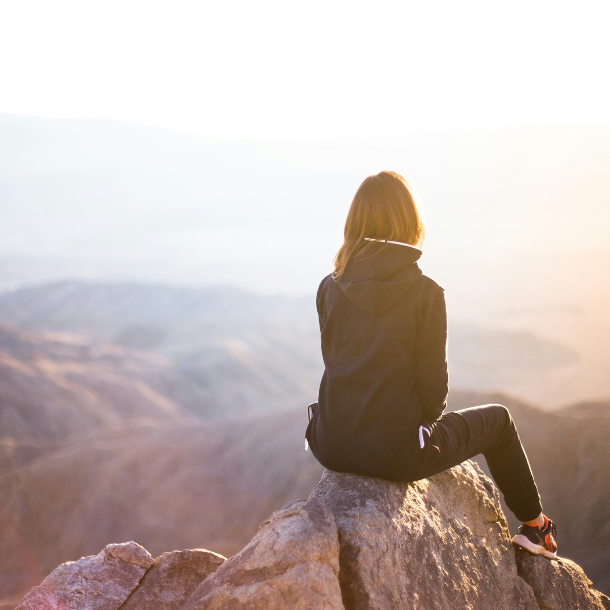 A woman sitting on a rock at sunrise, looking out over a wide valley